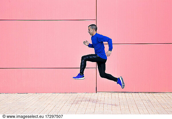 Sporty man exercising on fuchsia wall