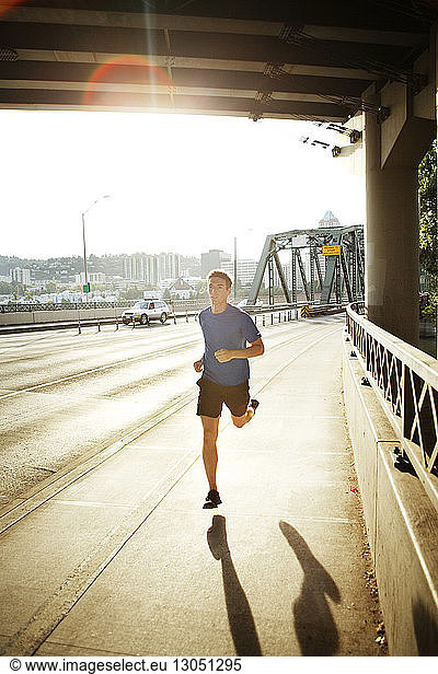 Sporty man jogging on bridge in city