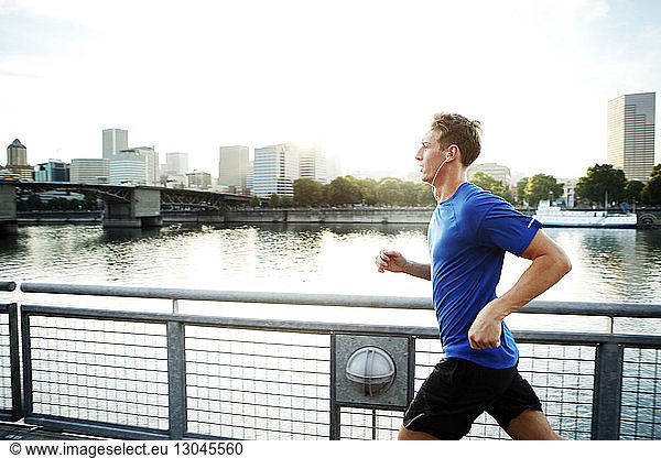 Sporty man jogging on promenade by river in city
