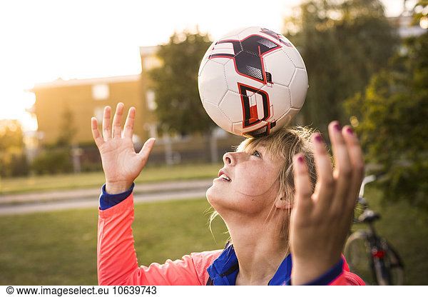 Sporty woman balancing soccer ball on forehead at park
