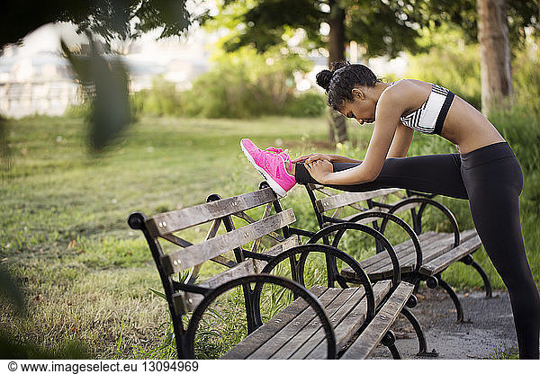 Sporty woman stretching leg on bench at park