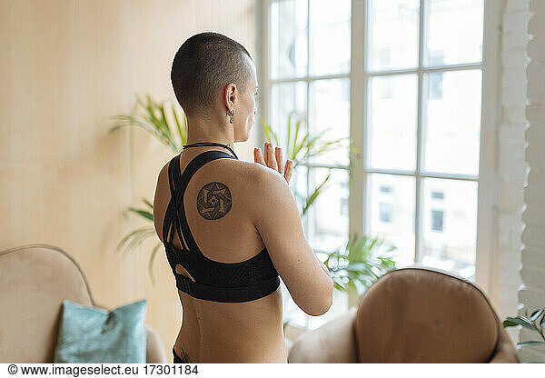sporty woman with ethnic tattoo meditating near window