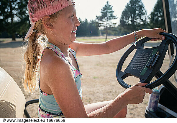 Sporty young girl making faces while driving golf cart on golf fairway