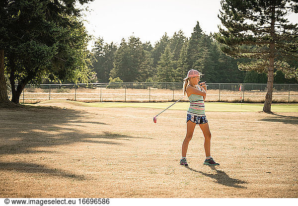 Sporty young girl with golf club standing on golf fairway