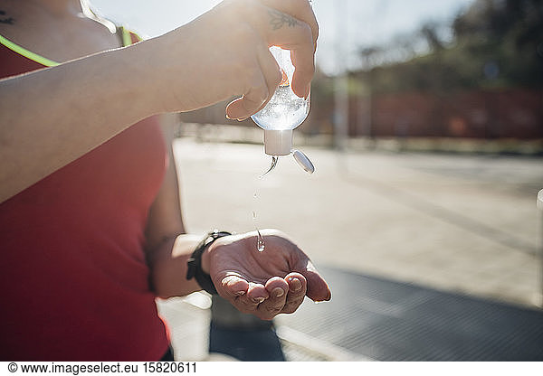 Sporty young woman in the city using sanitizer