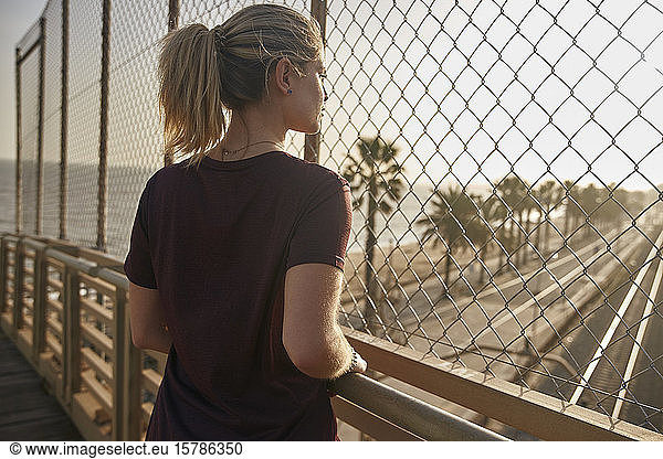 Sporty young woman standing on a bridge looking through a fence