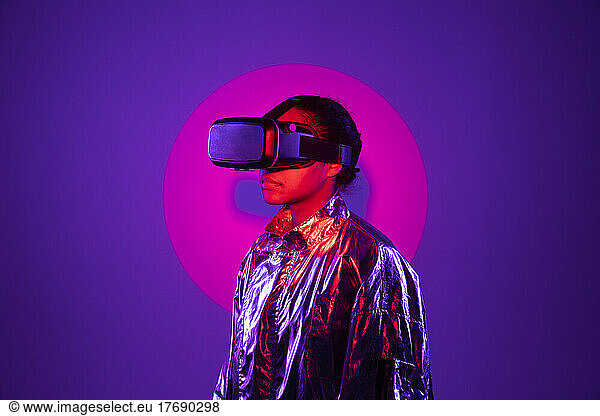Spotlight falling on woman wearing virtual reality simulator against purple background