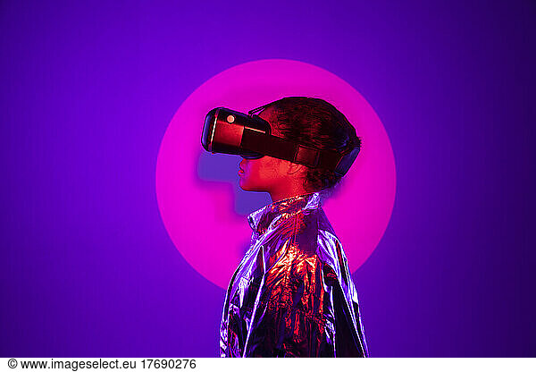 Spotlight falling on young woman wearing virtual reality simulator against purple background