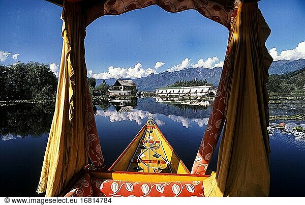 Srinagar  Jammu and Kashmir  India  Asia - A traditional wooden Shikara boat with its typical drapes and baldachin crosses the Dal Lake while the surrounding mountains and landscape is reflected on the water surface.