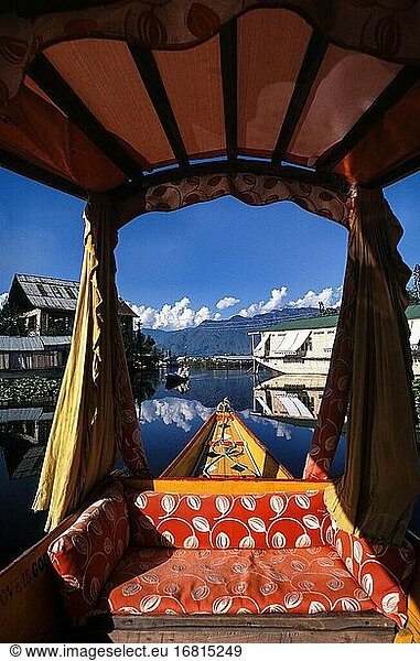 Srinagar  Jammu and Kashmir  India  Asia - A traditional wooden Shikara boat with its typical drapes and baldachin crosses the Dal Lake while the surrounding mountains and landscape is reflected on the water surface.