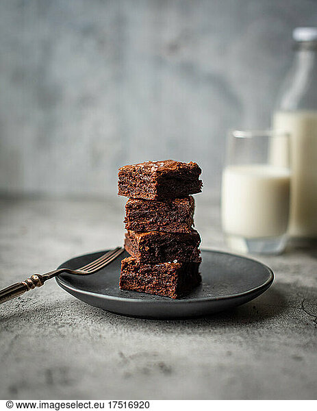 Stack of chocolate brownies on a plate with glass of milk.