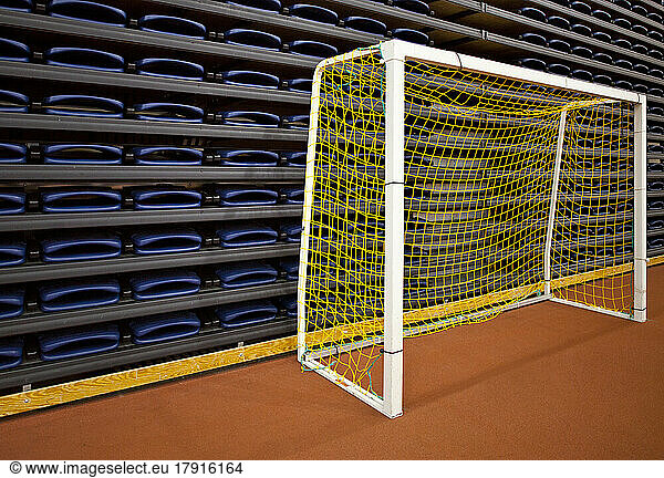 Stack of folded seats at an indoor sports venue  and a practise football goal net.