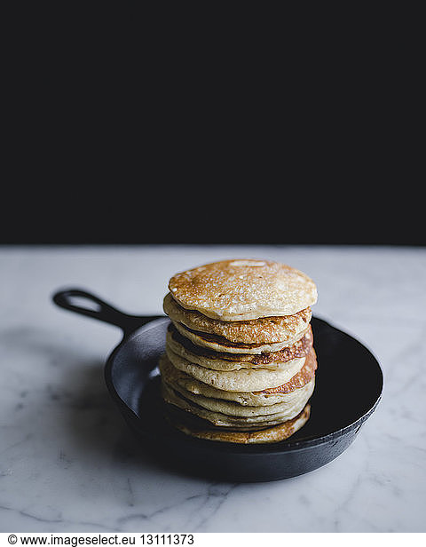 Stack of pancakes in frying pan on marble counter