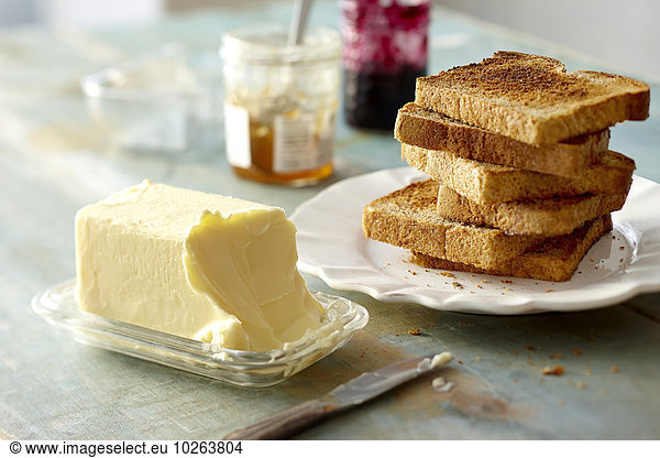Stack of Whole Wheat Toast on Plate with Block of Butter and Jam on Tabletop