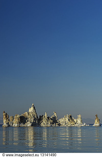 Stack rocks in sea against clear blue sky