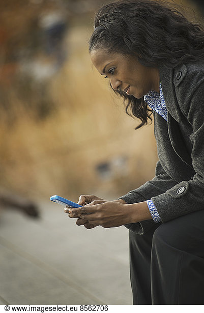 Stadtleben. Eine Frau im Mantel  Kontrolle und SMS  in Kontakt bleiben  ein Mobiltelefon benutzen.