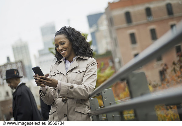 Stadtleben. Eine Frau im Mantel  Kontrolle und SMS  in Kontakt bleiben  ein Mobiltelefon benutzen.