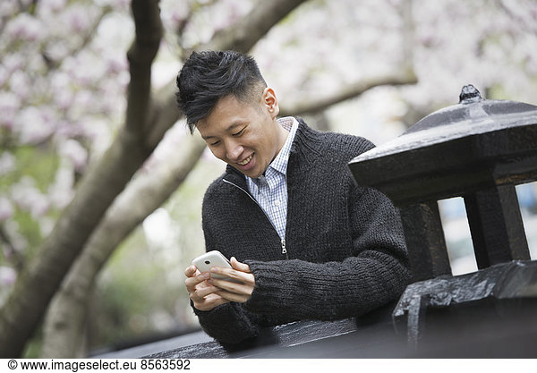 Stadtleben im Frühling. Ein junger Mann im Freien in einem Stadtpark. Sitzt auf einer Bank.