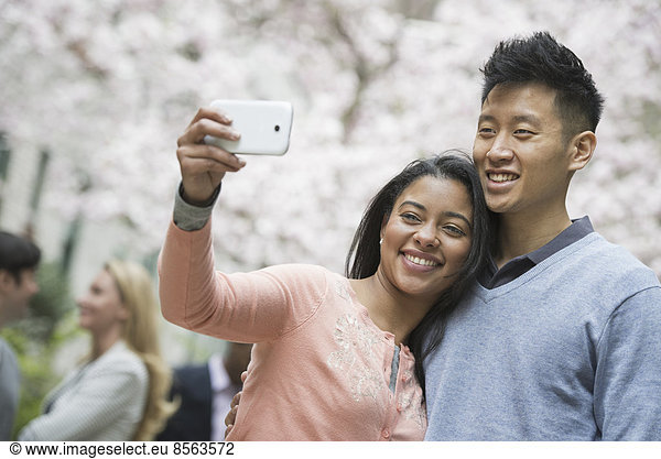 Stadtleben im Frühling. Jugendliche im Freien in einem Stadtpark. Ein Paar beim Selbstporträt oder Selbstporträt mit einem Smartphone.