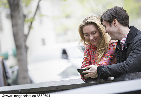 Stadtleben im Frühling. Jugendliche im Freien in einem Stadtpark. Zwei Menschen sitzen nebeneinander und schauen auf ein Smartphone.