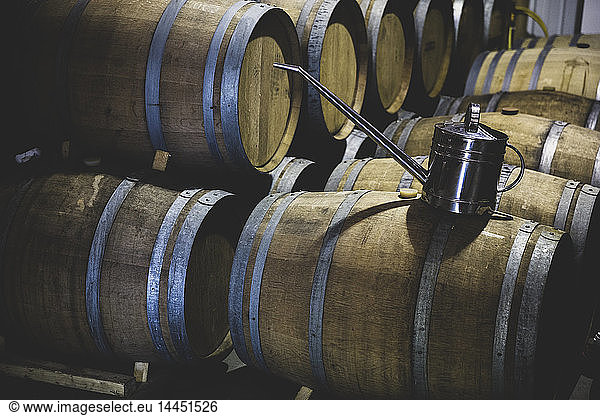 Stainless steel can on top of oak wood wine barrels in a cellar during the winemaking process.