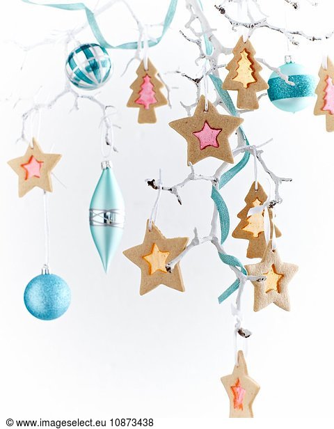 Star shaped stained glass biscuits and baubles hanging from painted white branch