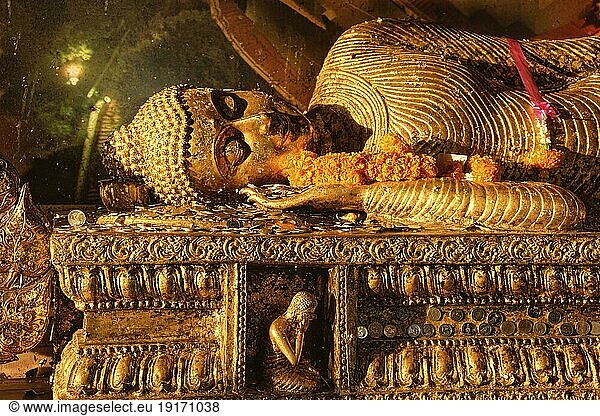 Statue des liegenden Buddha  bedeckt mit goldenen Blättern  Münzen und Blumengirlanden als Opfergaben im sanften Sonnenlicht. Traditionelles Bild  Rituale des Gebets  der Verehrung und des Segens. Buddhismus  Religion  Theravada  Thailand  heilig  Asien