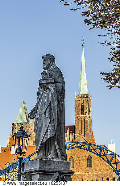 Statue of St. John the Baptist on Tumski Bridge with the Church of the Holy Cross (Collegiate Church of the Holy Cross and St. Bartholomew) in the background; Wroclaw  Silesia  Poland