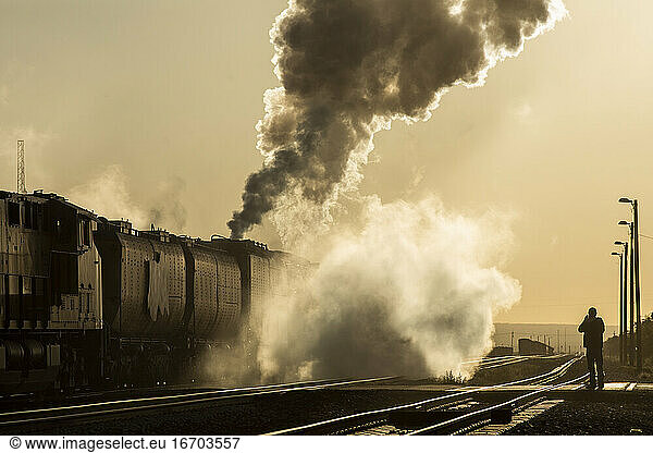 Steam engine smoking heavily moves down track into yellow sunrise