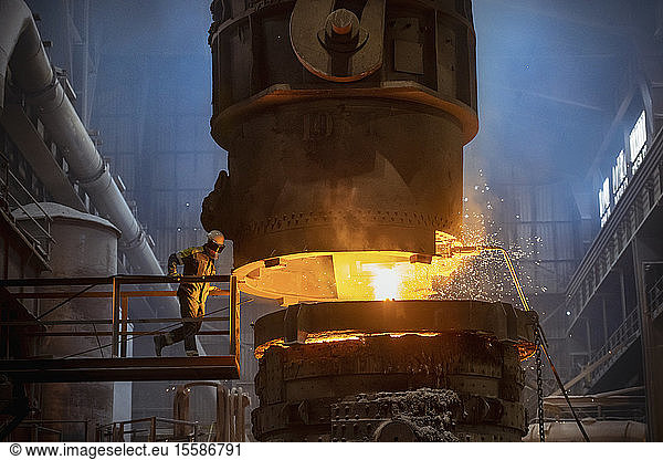 Steelworker inspecting molten steel during steel pour in steelworks