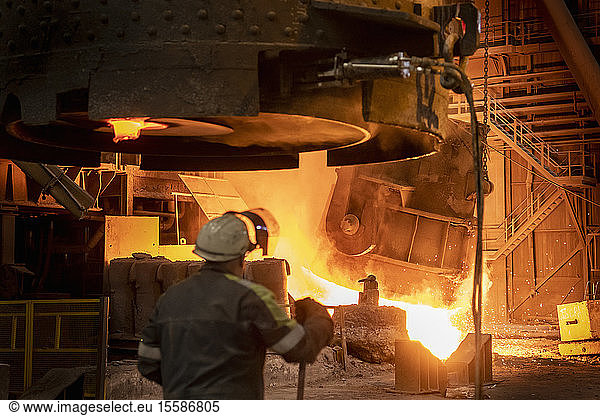 Steelworker looking on as molten steel flask is emptied during steel pour in steelworks