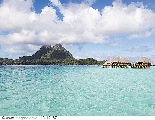 Stilt houses in lagoon of Bora Bora island against cloudy sky