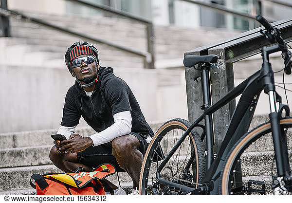 Stilvoller junger Mann mit Fahrrad  Smartphone und Kuriertasche in der Stadt