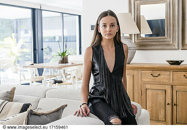 Stilvolles selbstbewusstes Teenager-Mädchen mit schwarzem Oberteil  das auf dem Sofa im Wohnzimmer sitzt