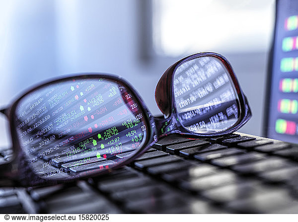 Stock market data reflecting in eyeglasses lying on laptop keyboard
