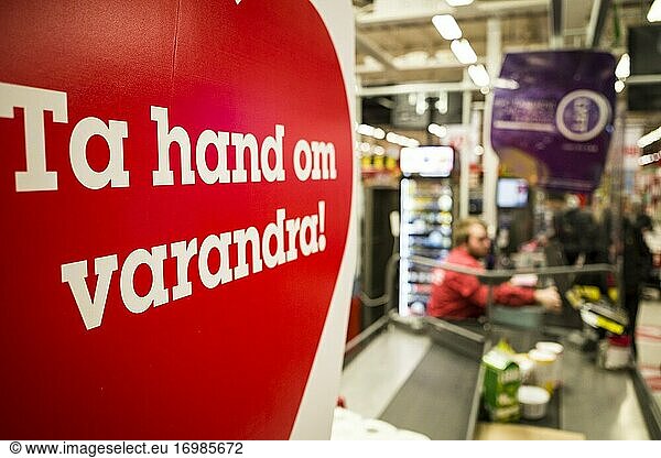 Stockholm  Schweden Menschen an der Kasse eines Willy:s-Supermarkts und eine Absperrung zwischen den Kunden  um die Verbreitung von Viren zu verhindern  mit der Aufschrift Passt aufeinander auf. '.