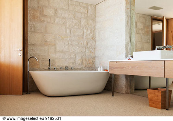 Stone wall behind soaking tub in modern bathroom