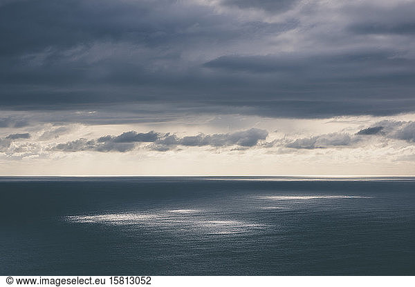 Storm clouds clearing over expansive ocean  dappled sunlight on the water