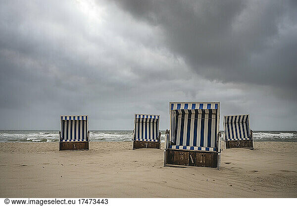 Storm clouds over hooded beach chairs standing on empty beach
