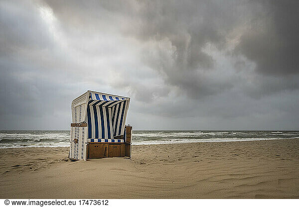 Storm clouds over lone hooded beach chair standing on empty beach