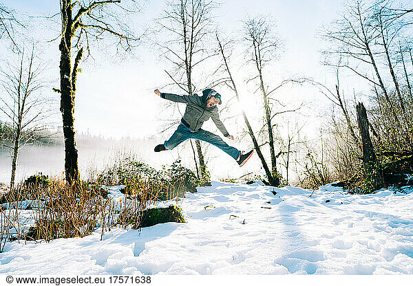 Straight on full length view of a man jumping off a log in winter