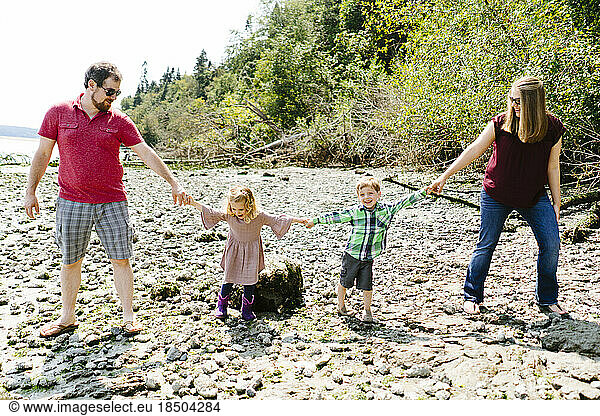 Straight on portrait of a family of four holding hands on a rocky beac