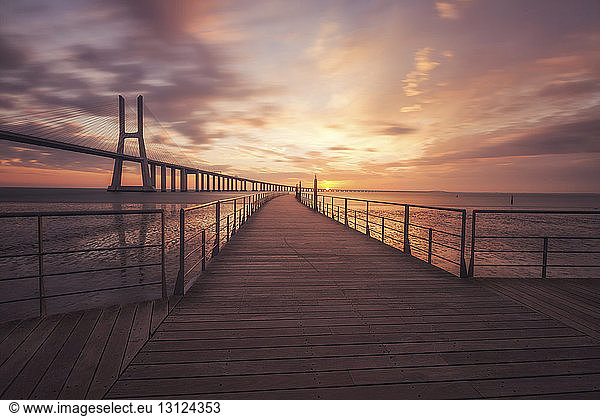 Strandpromenade an der Vasco-da-Gama-Brücke über den Tejo vor dramatischem Himmel bei Sonnenaufgang