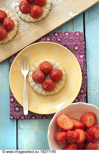 Strawberry tartlets on plate besides bowl of strawberry  close up
