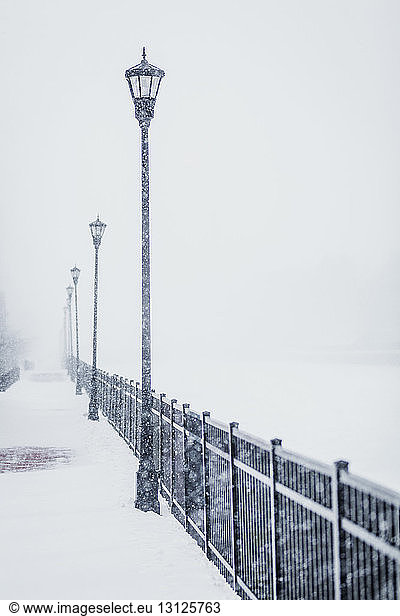 Street lights by metallic railing during snowfall
