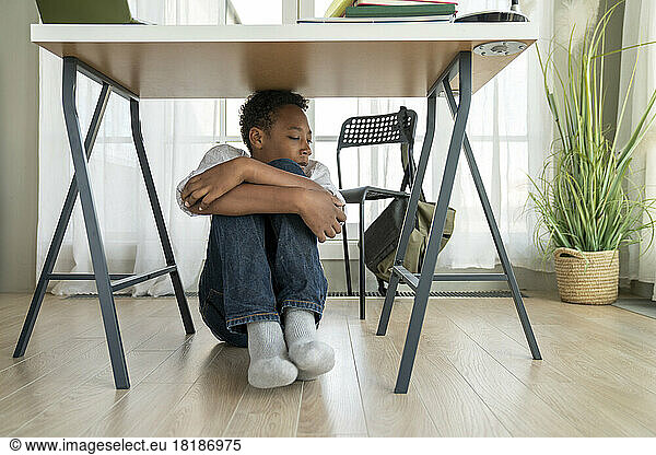 Stressed boy sitting under table at home