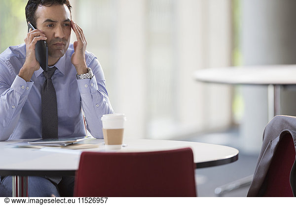 Stressed businessman talking on cell phone at table