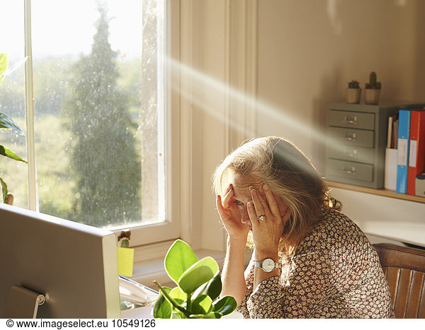 Stressed woman using computer in sunny home office