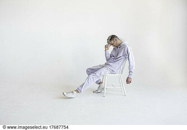 Stressed young man sitting on chair against white background