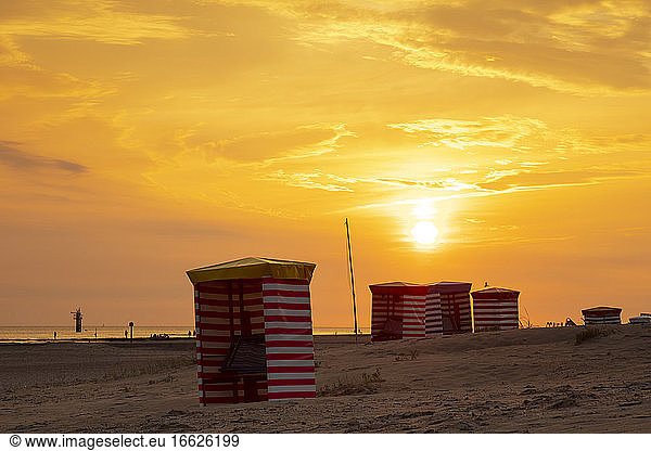 Striped tents at beach against orange sky during sunset